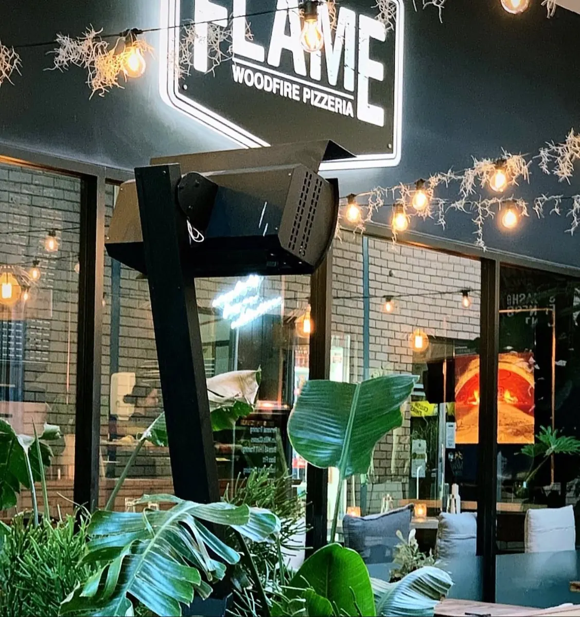 Flame Woodfire Pizzeria shopfront at night with the illuminated Flame sign